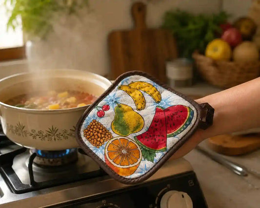 Hand holding colorful quilted cotton pot holder with fruit print design, soft padded kitchen hot pad.