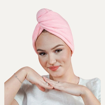 A woman wearing a light pink terry cloth hair wrap headband, styled in a twisted bun, against a solid off-white background.