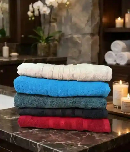 A stack of five folded cotton towels in different colors: cream, bright blue, dark teal, black, and red, set against a plain light gray background.