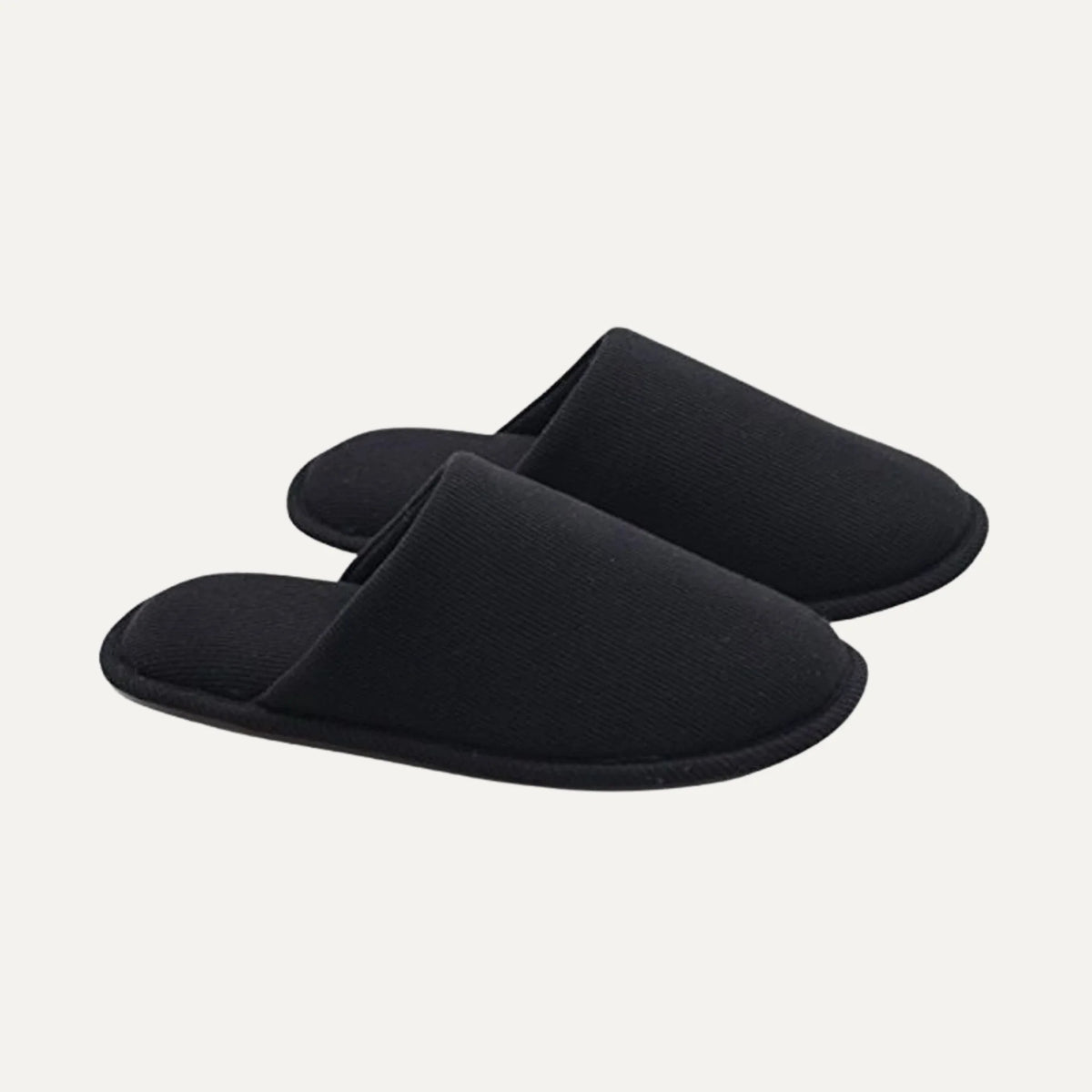 A pair of black slip-on slippers with a soft, textured fabric upper and matching sole, shown on a light off-white background.