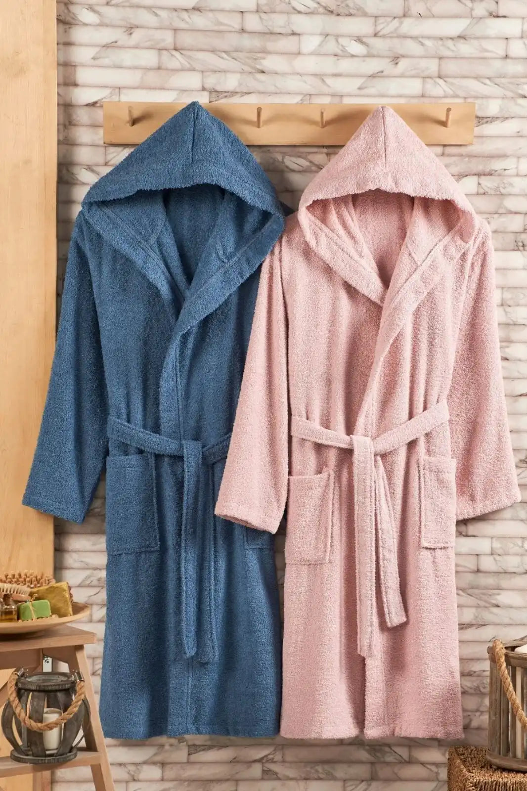 Blue and pink hooded robes hanging on a wooden rod against a stone wall.