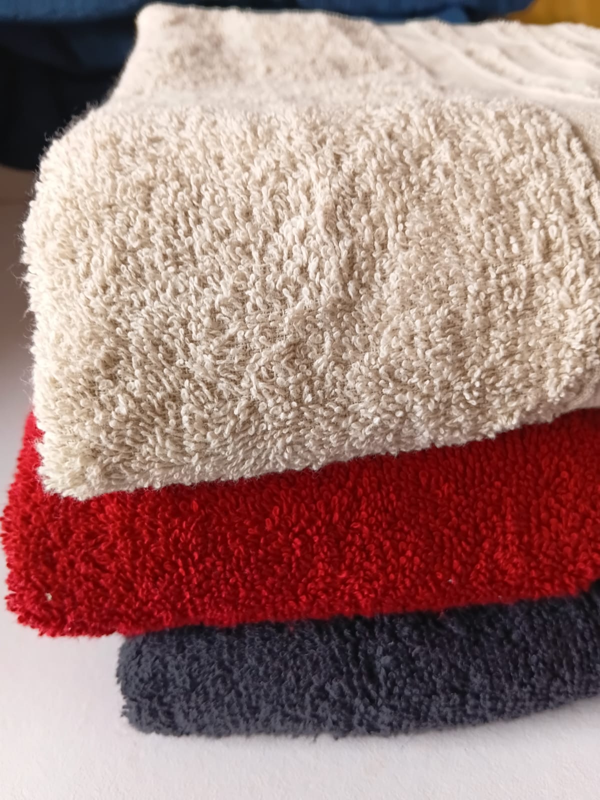 Stack of three textured towels in beige, red, and gray on a white surface.